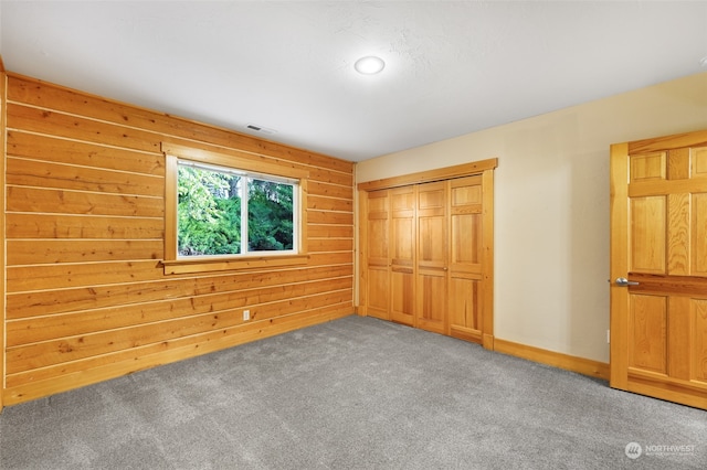 unfurnished bedroom with wooden walls, carpet, and a closet