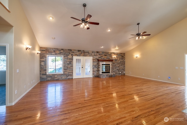 unfurnished living room with a stone fireplace, light hardwood / wood-style flooring, high vaulted ceiling, and ceiling fan