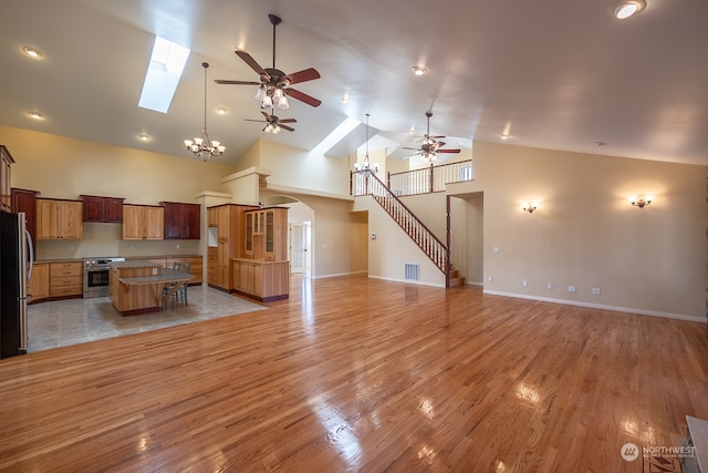 living room with ceiling fan with notable chandelier, high vaulted ceiling, light wood-type flooring, and a skylight