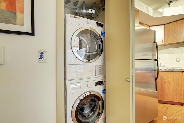 laundry area with stacked washer / drying machine and light hardwood / wood-style floors