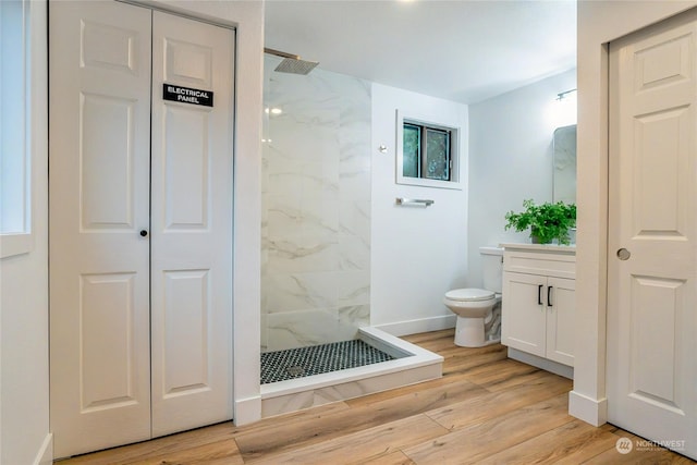 bathroom featuring hardwood / wood-style flooring, tiled shower, vanity, and toilet