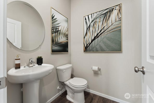 half bathroom with a sink, baseboards, toilet, and wood finished floors