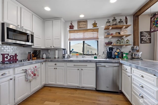 kitchen featuring appliances with stainless steel finishes, light wood-type flooring, decorative backsplash, and white cabinets