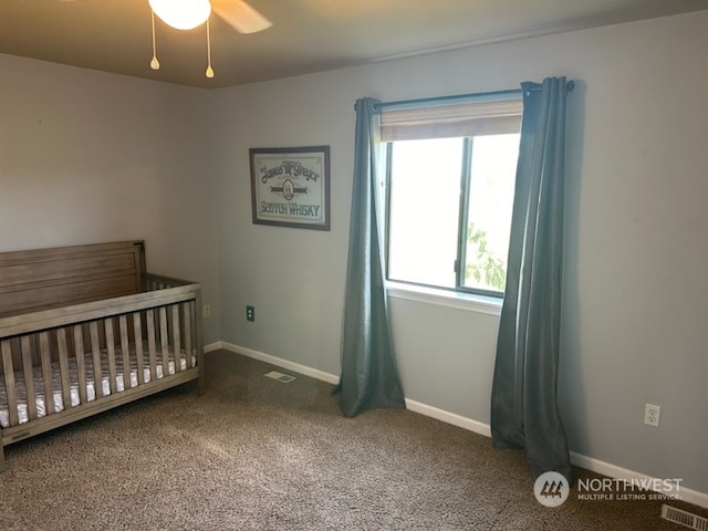 unfurnished bedroom with dark carpet, a crib, and ceiling fan