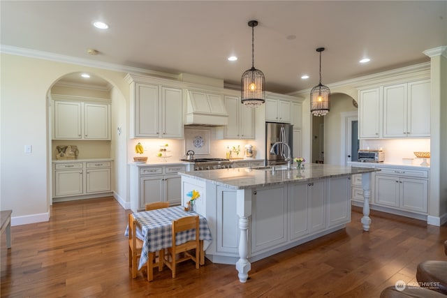 kitchen featuring wood-type flooring, appliances with stainless steel finishes, pendant lighting, custom exhaust hood, and a center island with sink