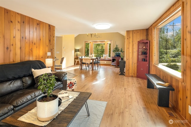 living room featuring light hardwood / wood-style floors, a wealth of natural light, wooden walls, and a chandelier