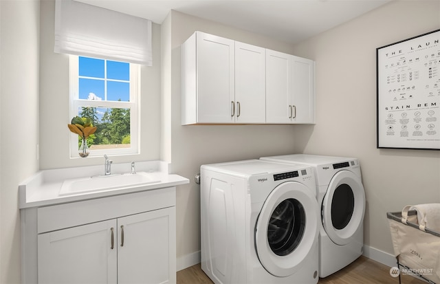 clothes washing area featuring sink, light hardwood / wood-style flooring, independent washer and dryer, and cabinets