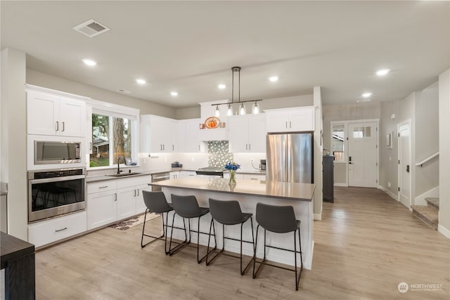 kitchen featuring a kitchen island, appliances with stainless steel finishes, sink, white cabinets, and hanging light fixtures