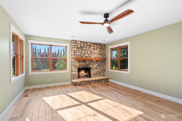 unfurnished living room with a stone fireplace, light hardwood / wood-style flooring, a textured ceiling, and ceiling fan