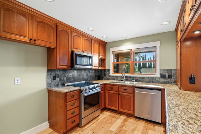 kitchen featuring tasteful backsplash, light stone countertops, appliances with stainless steel finishes, sink, and light wood-type flooring