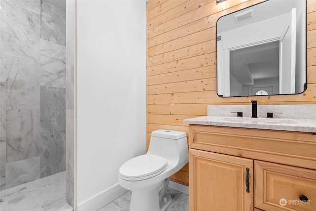 bathroom featuring vanity, toilet, wood walls, and tiled shower