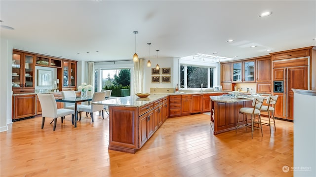 kitchen with light stone countertops, decorative light fixtures, a kitchen island, and light hardwood / wood-style floors