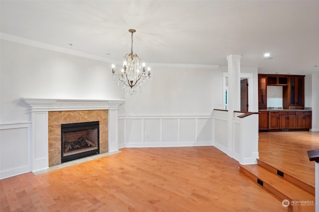 unfurnished living room featuring a high end fireplace, a notable chandelier, and light wood-type flooring