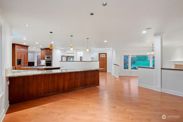 kitchen with hanging light fixtures, light hardwood / wood-style flooring, light stone countertops, kitchen peninsula, and a chandelier