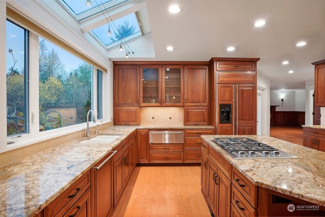 kitchen featuring sink, paneled refrigerator, light stone counters, lofted ceiling with skylight, and stainless steel gas stovetop