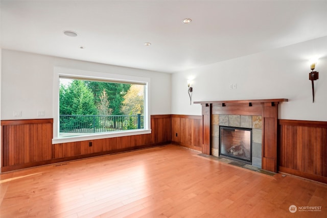 unfurnished living room with a fireplace, wooden walls, and light hardwood / wood-style flooring