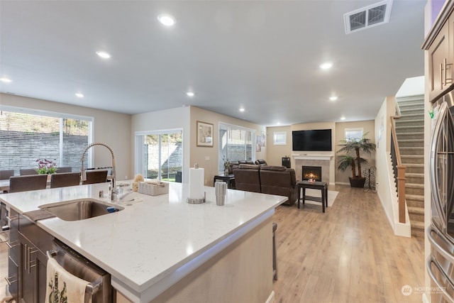 kitchen with light stone countertops, sink, an island with sink, light hardwood / wood-style floors, and stainless steel appliances