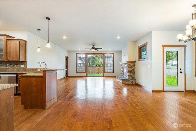 kitchen featuring sink, light stone counters, decorative light fixtures, ceiling fan with notable chandelier, and hardwood / wood-style flooring