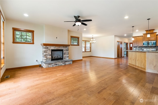 unfurnished living room featuring a fireplace, light wood-type flooring, ceiling fan with notable chandelier, and sink