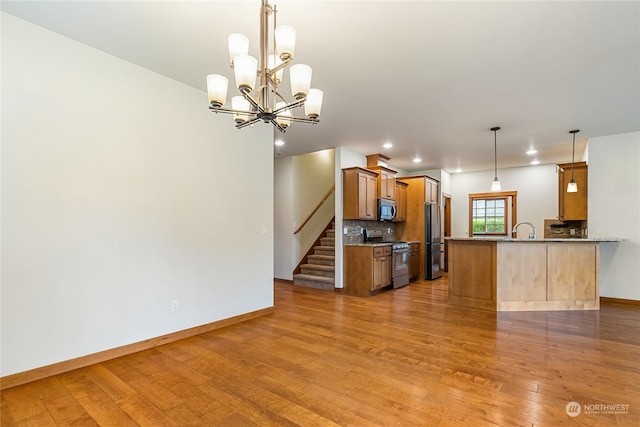 kitchen with kitchen peninsula, appliances with stainless steel finishes, light wood-type flooring, a notable chandelier, and hanging light fixtures