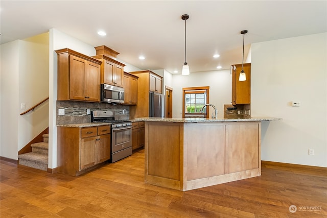 kitchen with kitchen peninsula, appliances with stainless steel finishes, light wood-type flooring, light stone counters, and pendant lighting