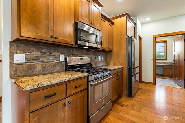 kitchen featuring decorative backsplash, light stone counters, light wood-type flooring, and appliances with stainless steel finishes