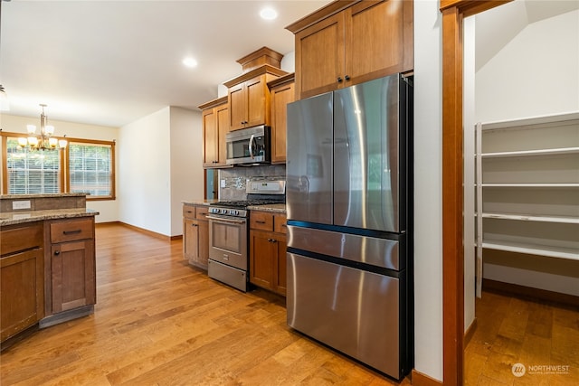 kitchen with backsplash, light hardwood / wood-style flooring, light stone counters, stainless steel appliances, and a chandelier