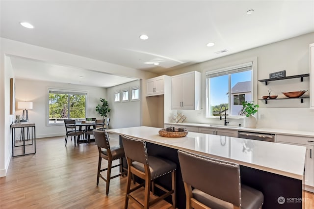 kitchen with sink, light wood-type flooring, a kitchen island, a kitchen breakfast bar, and white cabinets