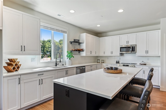 kitchen featuring a kitchen island, a kitchen breakfast bar, sink, white cabinets, and appliances with stainless steel finishes