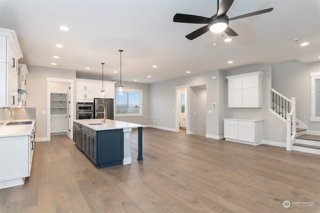 kitchen with appliances with stainless steel finishes, white cabinets, hanging light fixtures, and an island with sink