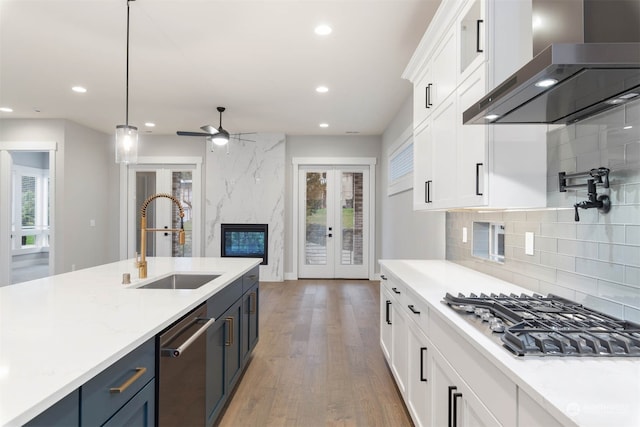 kitchen with wall chimney range hood, white cabinets, sink, and hanging light fixtures