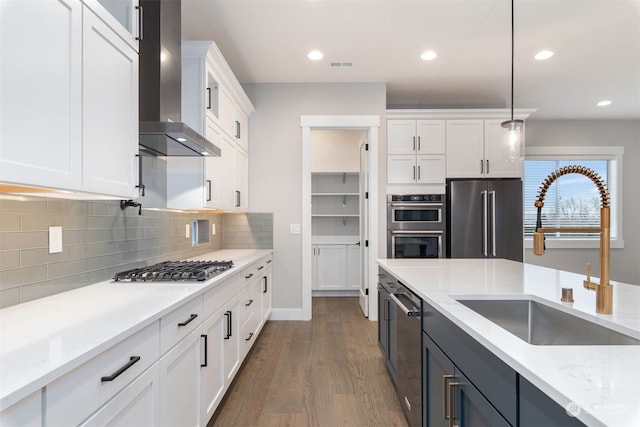 kitchen with wall chimney exhaust hood, white cabinets, stainless steel appliances, and decorative light fixtures