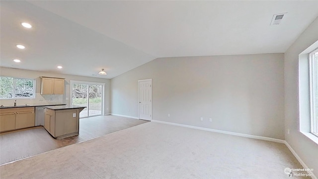 kitchen featuring light colored carpet, tasteful backsplash, light brown cabinetry, vaulted ceiling, and stainless steel dishwasher