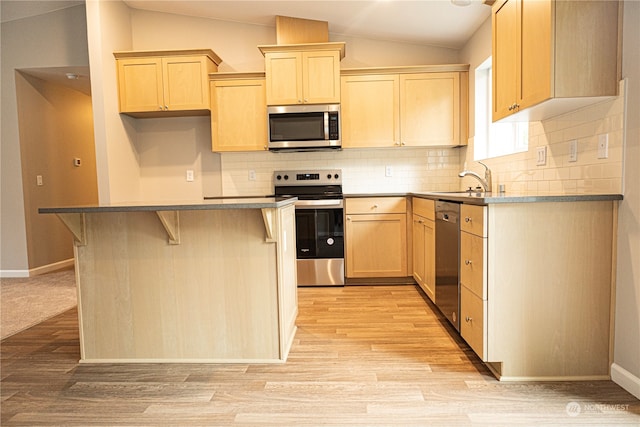 kitchen featuring lofted ceiling, appliances with stainless steel finishes, a center island, and light brown cabinetry