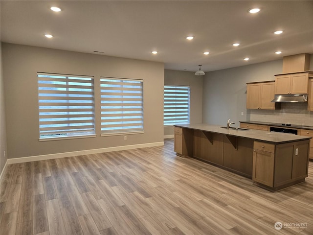 kitchen featuring sink, light hardwood / wood-style flooring, an island with sink, decorative backsplash, and light brown cabinets