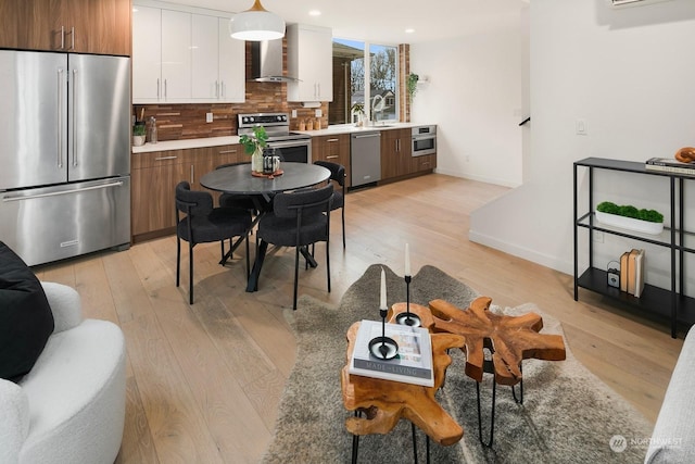 kitchen with tasteful backsplash, white cabinetry, light hardwood / wood-style floors, stainless steel appliances, and wall chimney exhaust hood