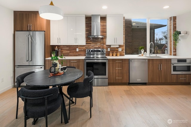 kitchen with appliances with stainless steel finishes, pendant lighting, white cabinetry, sink, and wall chimney exhaust hood