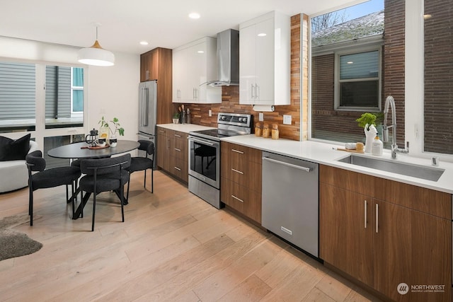 kitchen with wall chimney exhaust hood, sink, white cabinetry, hanging light fixtures, and stainless steel appliances