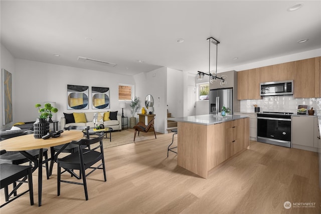 kitchen featuring a center island, a breakfast bar, pendant lighting, light wood-type flooring, and appliances with stainless steel finishes