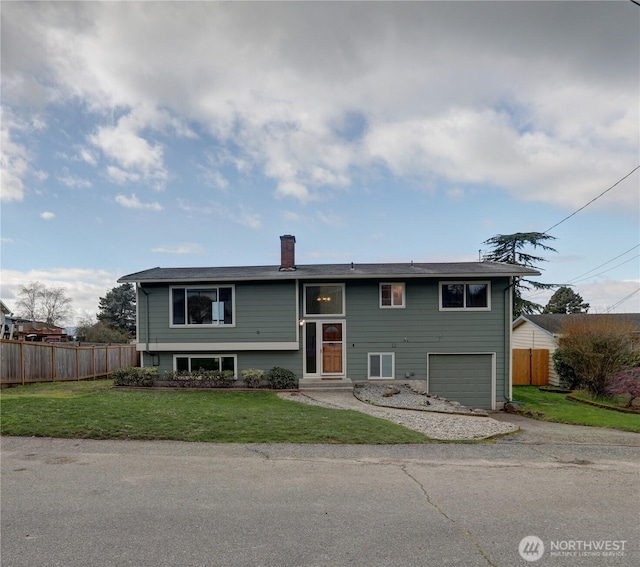 raised ranch featuring a front yard, fence, a chimney, and an attached garage