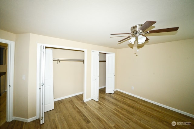 unfurnished bedroom featuring ceiling fan, wood-type flooring, and two closets