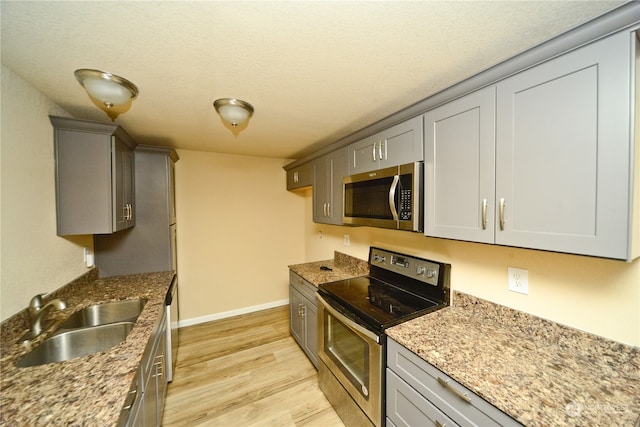 kitchen featuring appliances with stainless steel finishes, sink, a textured ceiling, light hardwood / wood-style floors, and light stone counters