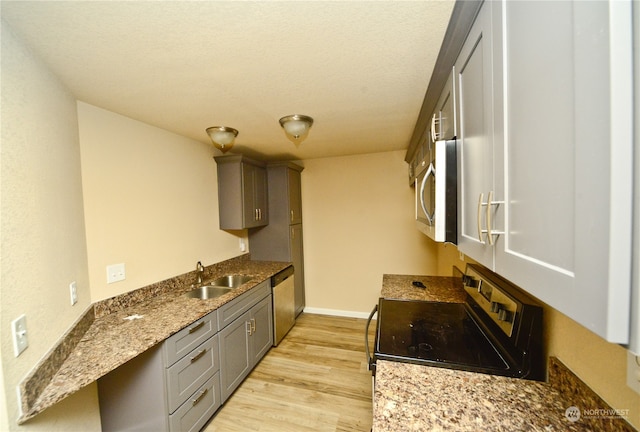 kitchen with light stone counters, appliances with stainless steel finishes, light wood-type flooring, gray cabinetry, and sink