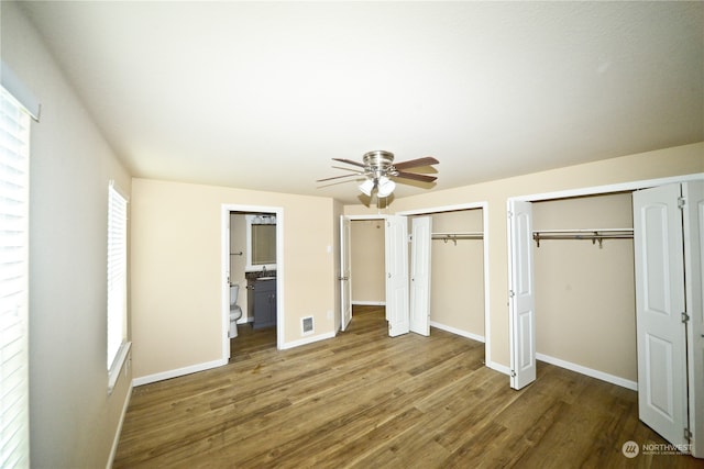 unfurnished bedroom featuring connected bathroom, multiple closets, wood-type flooring, and ceiling fan