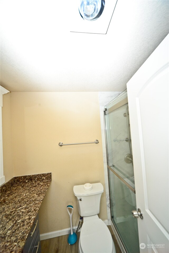 bathroom featuring vanity, a shower with shower door, hardwood / wood-style flooring, and toilet