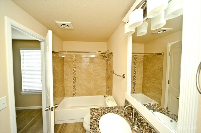 full bathroom with a textured ceiling, hardwood / wood-style flooring, toilet, vanity, and tiled shower / bath combo