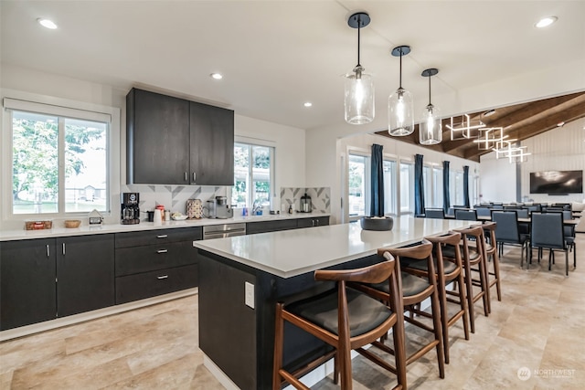 kitchen with a breakfast bar area, a kitchen island, dark cabinets, light countertops, and open floor plan