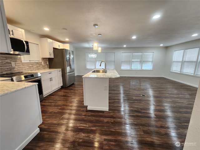 kitchen with hanging light fixtures, appliances with stainless steel finishes, white cabinetry, a kitchen island with sink, and sink