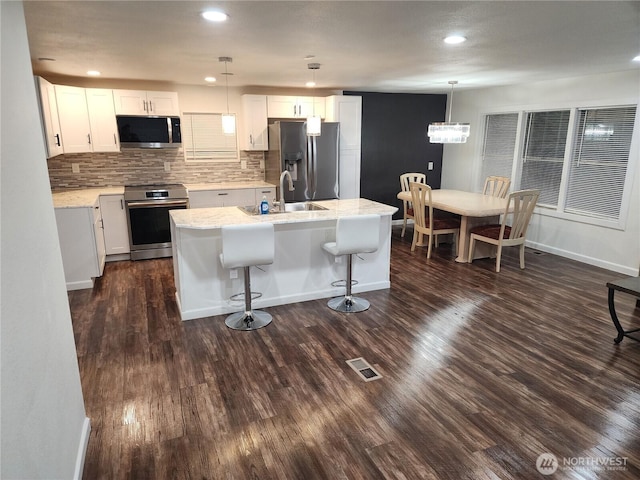 kitchen featuring visible vents, dark wood-type flooring, an island with sink, a sink, and stainless steel appliances