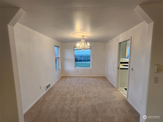 carpeted spare room with an inviting chandelier